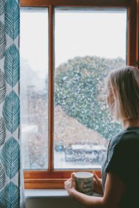 woman watching snow fall outside window